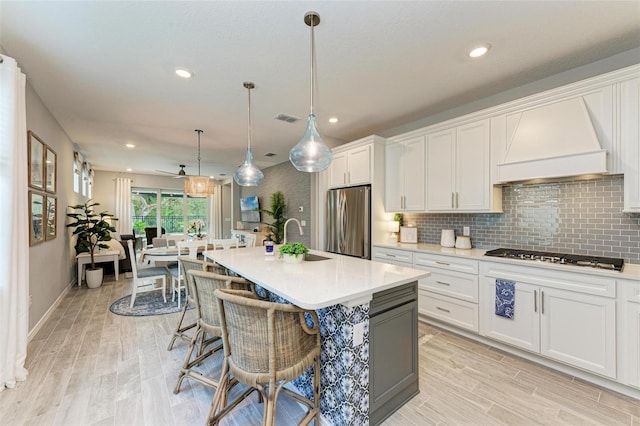 kitchen with appliances with stainless steel finishes, custom exhaust hood, white cabinetry, and an island with sink