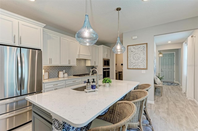 kitchen featuring a center island with sink, sink, white cabinets, appliances with stainless steel finishes, and light hardwood / wood-style floors