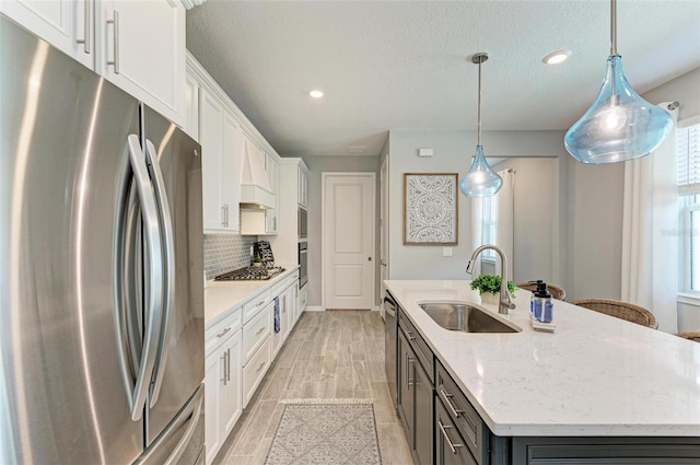 kitchen with appliances with stainless steel finishes, sink, a center island with sink, and hanging light fixtures