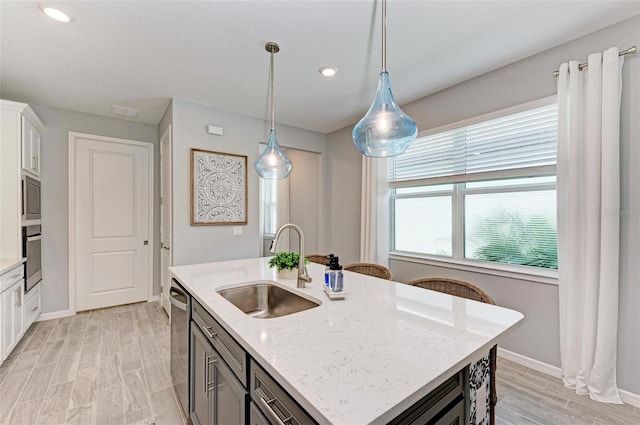 kitchen with white cabinetry, light wood-type flooring, light stone countertops, and an island with sink