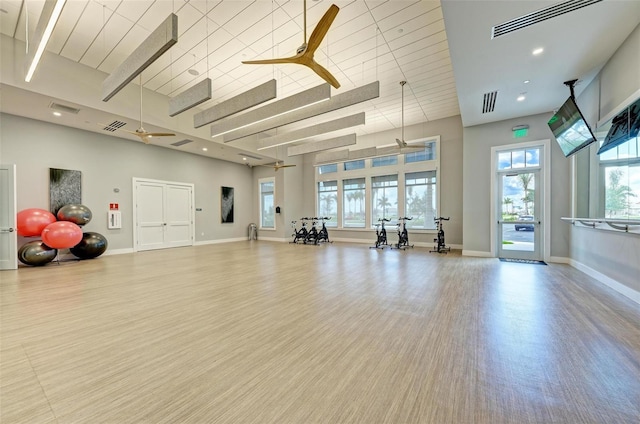 gym with wood-type flooring, a towering ceiling, and ceiling fan