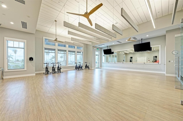 exercise room featuring ceiling fan, light hardwood / wood-style flooring, and a high ceiling