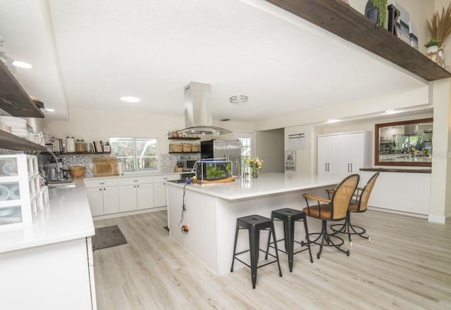 kitchen featuring island range hood, a breakfast bar area, a center island, light wood-type flooring, and white cabinets