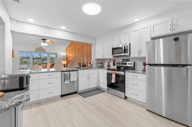 kitchen with light wood-style flooring, appliances with stainless steel finishes, white cabinetry, light stone countertops, and a peninsula