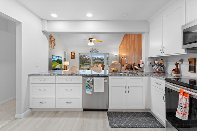 kitchen with a peninsula, light stone countertops, stainless steel appliances, white cabinetry, and a sink