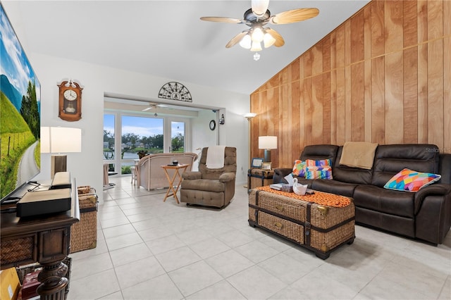 living room featuring a ceiling fan, vaulted ceiling, wooden walls, and light tile patterned floors