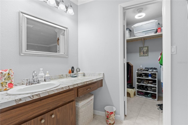 bathroom featuring tile patterned flooring, baseboards, a walk in closet, and vanity