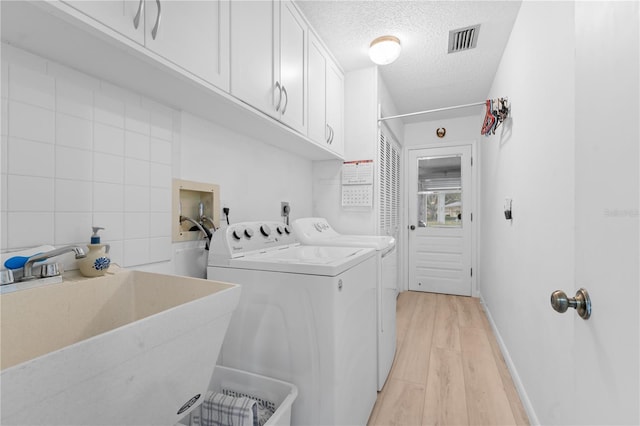 laundry room featuring cabinet space, visible vents, a textured ceiling, washer and dryer, and a sink