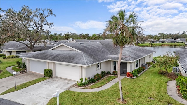 ranch-style house with a garage, a water view, driveway, roof with shingles, and a front lawn