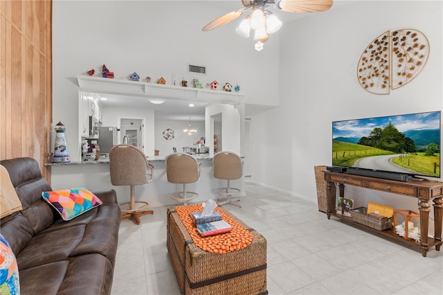 living area featuring light tile patterned floors, a towering ceiling, baseboards, visible vents, and a ceiling fan