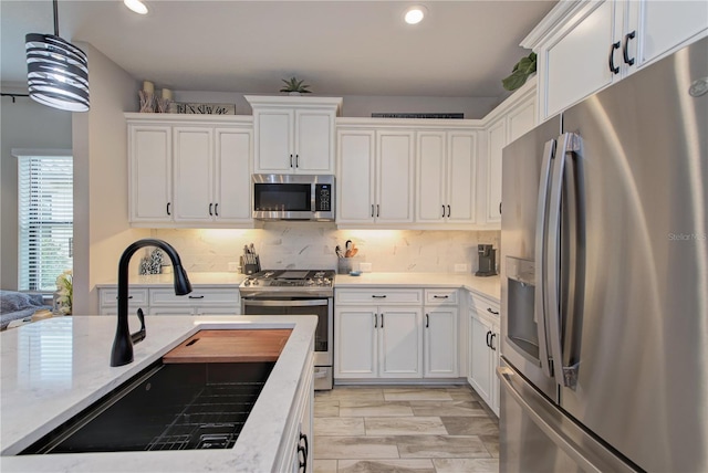 kitchen with tasteful backsplash, appliances with stainless steel finishes, sink, hanging light fixtures, and white cabinetry