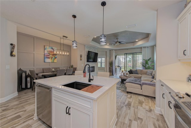 kitchen featuring light hardwood / wood-style flooring, a tray ceiling, a center island with sink, sink, and white cabinetry