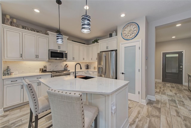 kitchen with appliances with stainless steel finishes, sink, hanging light fixtures, white cabinets, and a kitchen island with sink