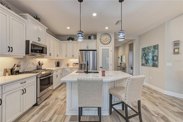 kitchen with an island with sink, decorative light fixtures, stainless steel appliances, and light hardwood / wood-style floors