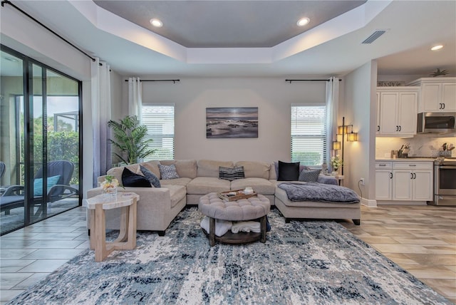 living room featuring light hardwood / wood-style flooring, a tray ceiling, and plenty of natural light