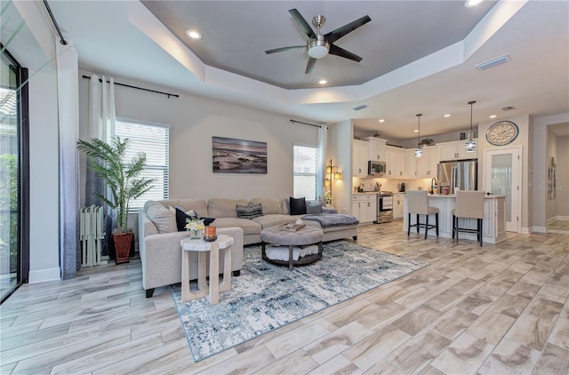 living room featuring a healthy amount of sunlight, ceiling fan, and a raised ceiling