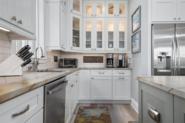 kitchen featuring white cabinets, stainless steel appliances, light stone counters, and backsplash