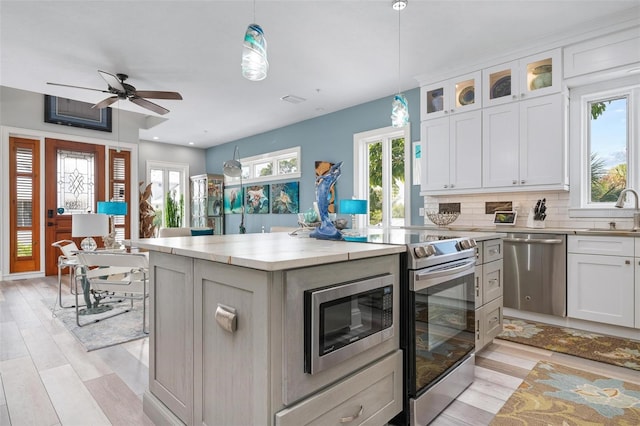 kitchen with white cabinetry, hanging light fixtures, stainless steel appliances, and a healthy amount of sunlight