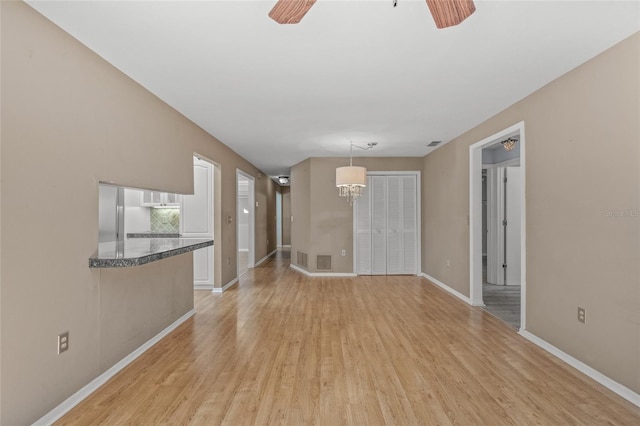 unfurnished living room featuring ceiling fan with notable chandelier and light hardwood / wood-style floors