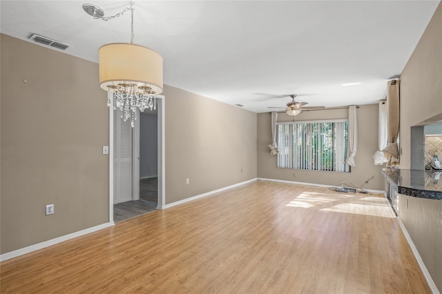 unfurnished living room featuring ceiling fan with notable chandelier and light hardwood / wood-style floors