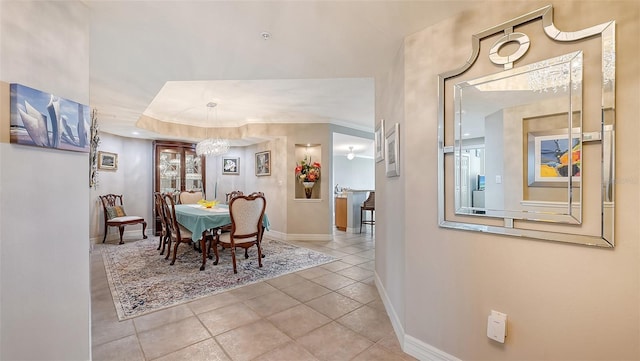 tiled dining room featuring a tray ceiling and an inviting chandelier