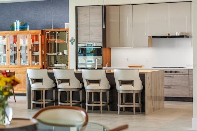 kitchen with double oven, light hardwood / wood-style flooring, a kitchen bar, and electric stovetop