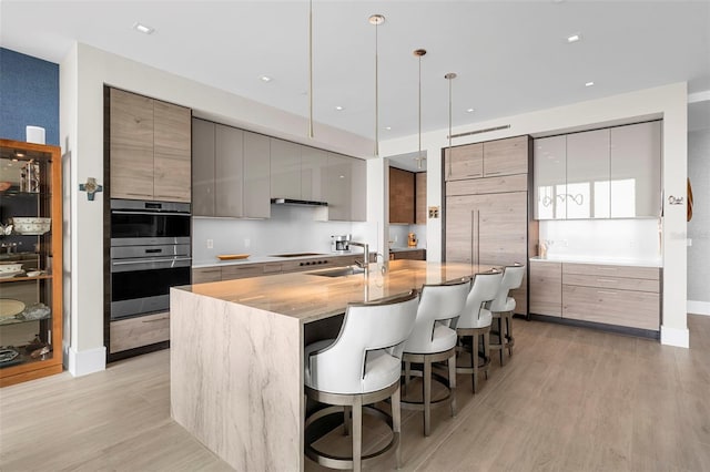 kitchen with sink, an island with sink, a kitchen breakfast bar, hanging light fixtures, and light hardwood / wood-style flooring