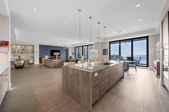 kitchen with a spacious island, sink, pendant lighting, a water view, and light hardwood / wood-style floors