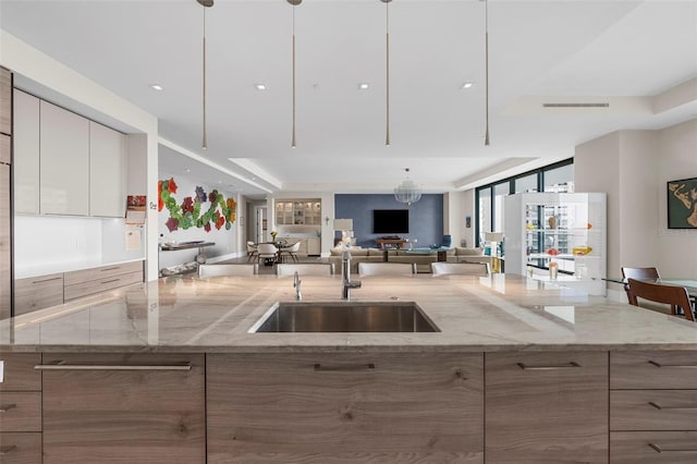 kitchen with a tray ceiling, light stone countertops, sink, and white cabinets