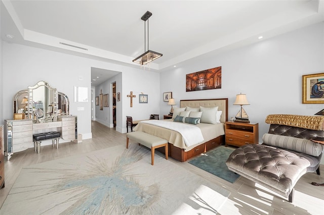 bedroom with a tray ceiling and light wood-type flooring