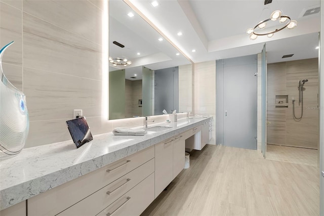 bathroom featuring a tray ceiling, tile walls, tiled shower, vanity, and hardwood / wood-style flooring