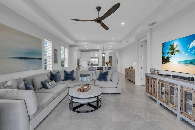 tiled living room with a tray ceiling and ceiling fan