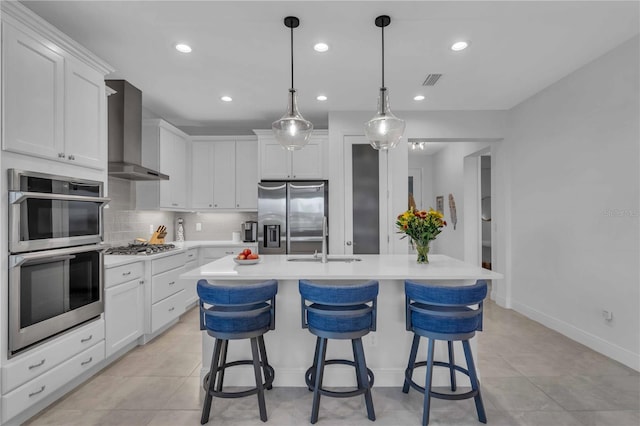 kitchen with a kitchen island with sink, wall chimney exhaust hood, stainless steel appliances, sink, and white cabinets