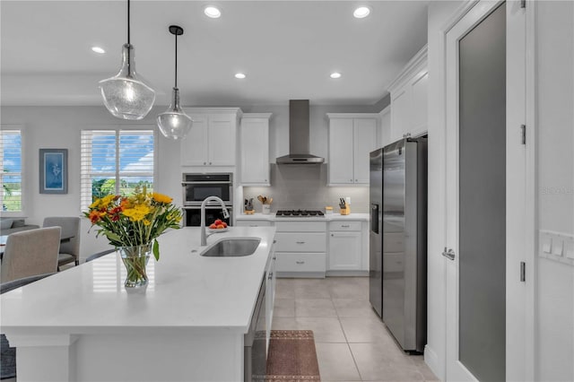 kitchen featuring white cabinets, a center island with sink, sink, wall chimney exhaust hood, and stainless steel appliances