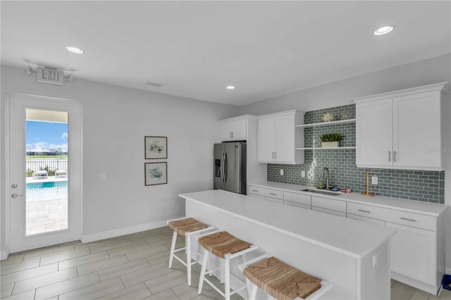 kitchen featuring stainless steel fridge, white cabinets, a kitchen island, a breakfast bar, and sink