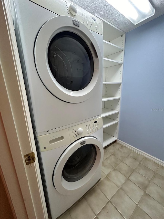 laundry room with a textured ceiling, light tile patterned flooring, and stacked washer and dryer