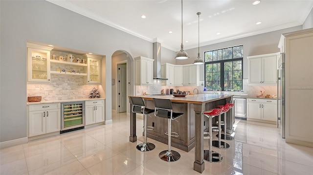 kitchen with beverage cooler, wall chimney range hood, a kitchen bar, decorative backsplash, and a kitchen island