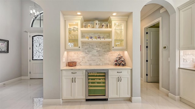 bar featuring backsplash, a notable chandelier, white cabinets, wine cooler, and hanging light fixtures