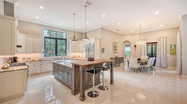 kitchen featuring light countertops, a center island with sink, hanging light fixtures, and built in refrigerator