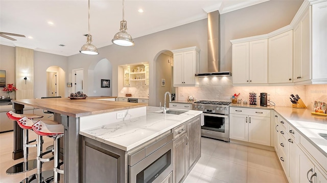 kitchen featuring high end stove, wall chimney exhaust hood, white cabinetry, and an island with sink