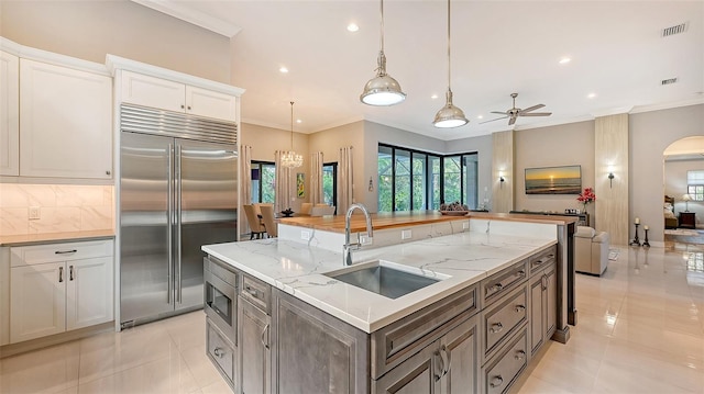 kitchen with stainless steel built in fridge, white cabinets, sink, pendant lighting, and a kitchen island with sink