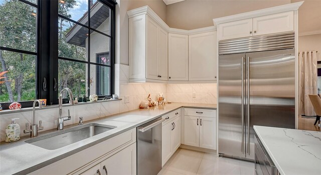 kitchen with stainless steel appliances, a sink, white cabinets, a wealth of natural light, and decorative backsplash