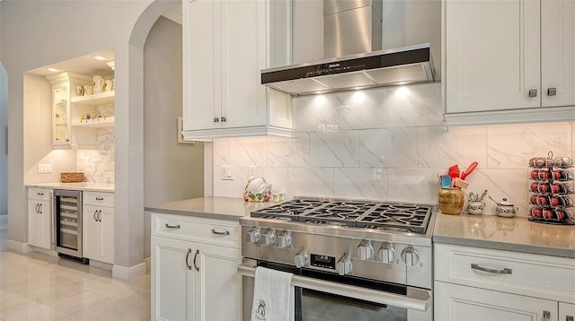 kitchen with range hood, open shelves, stainless steel range with gas stovetop, white cabinetry, and beverage cooler