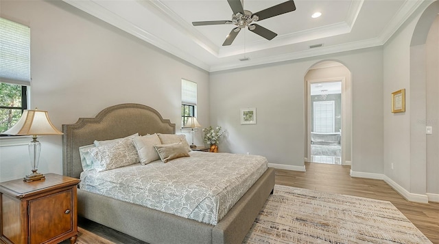 bedroom featuring light hardwood / wood-style floors, a raised ceiling, ceiling fan, and crown molding