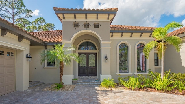 entrance to property featuring a garage, french doors, a tile roof, and stucco siding