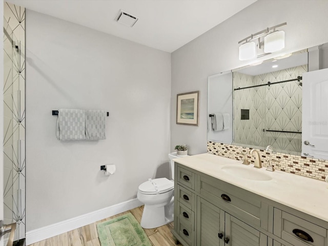 bathroom featuring tiled shower, toilet, hardwood / wood-style floors, vanity, and tasteful backsplash