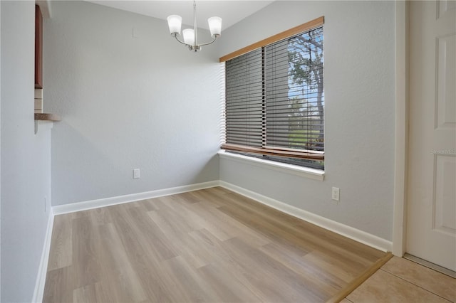 spare room with a chandelier and light wood-type flooring