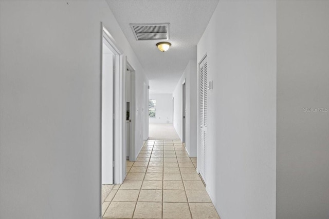 corridor featuring a textured ceiling and light tile patterned floors