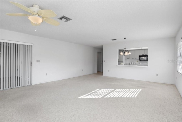 unfurnished living room with a textured ceiling, light colored carpet, and ceiling fan with notable chandelier