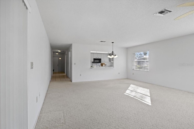 unfurnished living room with a textured ceiling, light colored carpet, and ceiling fan with notable chandelier